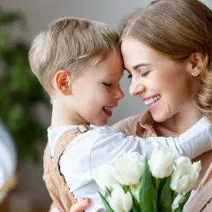 Uśmiechnięta mama i synek przytulają się, trzymając bukiet białych tulipanów. Idealny prezent na 26 maja, Dzień Matki.
