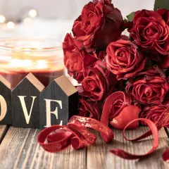 Bukiet czerwonych róż, świeca i ozdobne litery tworzące napis LOVE. Romantyczna sceneria na 11 rocznicę ślubu.