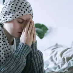 Osoba w chuście z kropkami modli się, szukając pocieszenia w modlitwie do św. Peregryna.