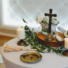 Ołtarz z krzyżem, świecami i kwiatami. Woda święcona i kropidło czekają na piękne błogosławieństwo.