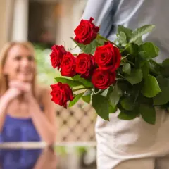 Bukiet czerwonych róż ukryty za plecami. Czy to niespodzianka na imieniny Klaudii?