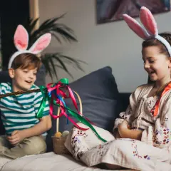 Dzieci w króliczych uszach cieszą się przerwą świąteczną wielkanocną, bawiąc się palmą i koszykiem z pisankami.