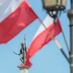Pomnik rycerza z mieczem i krzyżem na tle polskich flag i latarni.
