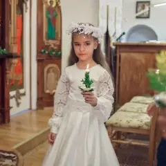Dziewczynka w białej sukni i wianku trzyma zapaloną świecę. To ważny dzień, w którym klasa przystępuje do komunii.