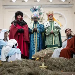Trzech króli w barwnych strojach przygląda się scenie narodzenia. Jeden z nich trzyma laskę, a obok leży żłóbek.