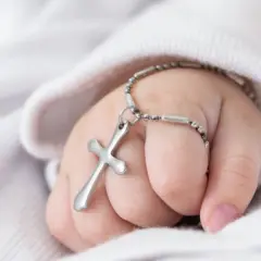 Dziecięca rączka z krzyżykiem na łańcuszku, symbol błogosławieństwa podczas chrztu dziecka.