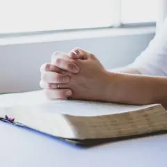 Dłonie złożone w modlitwie nad otwartą Biblią. To chwila głębokiej wiary i modlitwa o zdrowie dziecka.
