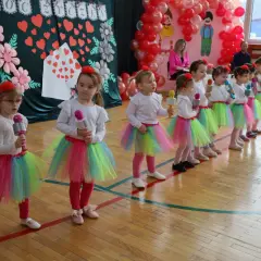 Dzieci w kolorowych spódniczkach śpiewają piosenkę na Dzień Dziecka, trzymając w rękach mikrofony.