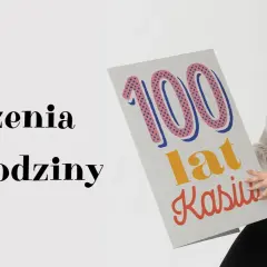 Kobieta z uśmiechem prezentuje kartkę z napisem "100 lat Kasiu!". To idealne śmieszne życzenia urodzinowe dla solenizantki.