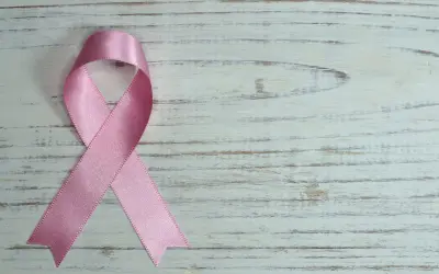Różowa wstążka na białym, drewnianym tle. Symbol nadziei i wsparcia, przypominający o mądrych słowach otuchy w chorobie.