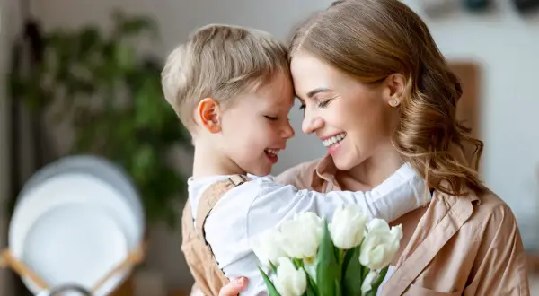 Uśmiechnięta mama i synek przytulają się, trzymając bukiet białych tulipanów. Idealny prezent na 26 maja, Dzień Matki.