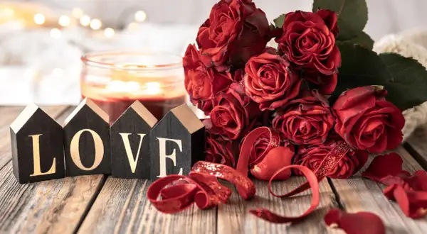 Bukiet czerwonych róż, świeca i ozdobne litery tworzące napis LOVE. Romantyczna sceneria na 11 rocznicę ślubu.