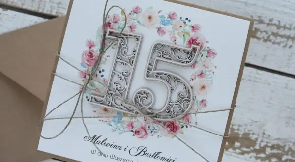 Elegancka kartka z napisem "15 rocznica ślubu" dla Malwiny i Bartłomieja, ozdobiona kwiatowym wianuszkiem i przewiązana sznurkiem.