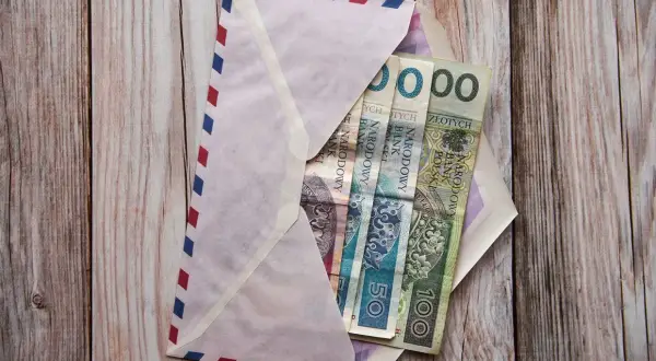 Koperta z polskimi banknotami (50 zł, 100 zł) na drewnianym tle.