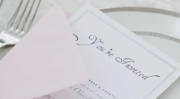 Eleganckie zaproszenie z napisem "You're Invited" i różową kopertą. Wskazówka, jak pisać na zaproszeniu z osobą towarzyszącą.