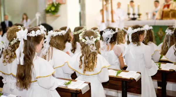 Dziewczynki w bieli, z wiankami na głowach, czekają na uroczystość. Krótkie życzenia na komunię dla nich.