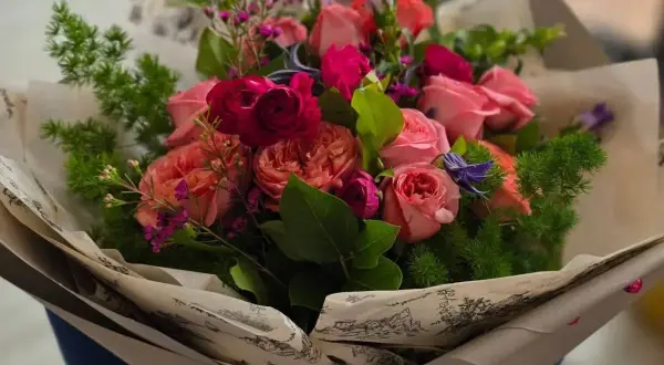 Piękny bukiet różowych i czerwonych róż, ozdobiony zielenią i drobnymi fioletowymi kwiatkami. Idealne kwiaty dla mamy, by sprawić jej radość.
