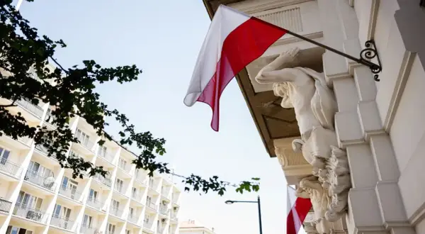 Biało-czerwona flaga powiewa na tle jasnego nieba, obok rzeźb atlantesów. Czy 2 maja jest wolny?