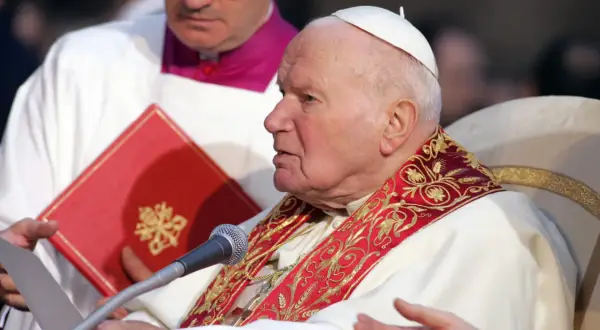 Papież Jan Paweł II podczas modlitwy do Ducha Świętego o uzdrowienie. W rękach trzyma dokument i czerwoną księgę.