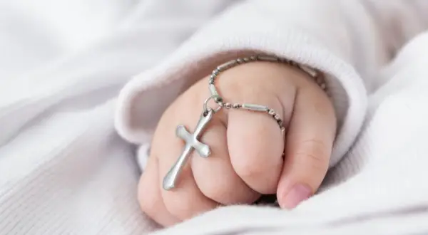 Dziecięca rączka z krzyżykiem na łańcuszku, symbol błogosławieństwa podczas chrztu dziecka.