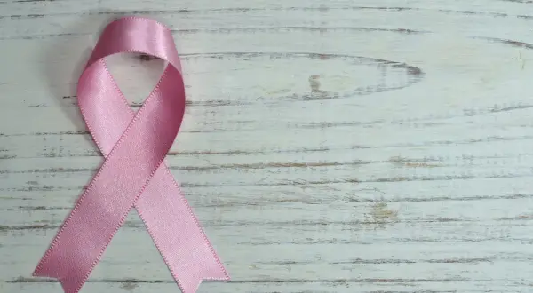 Różowa wstążka na białym, drewnianym tle. Symbol nadziei i wsparcia, przypominający o mądrych słowach otuchy w chorobie.