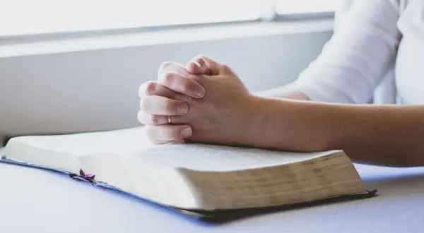 Dłonie złożone w modlitwie nad otwartą Biblią. To chwila głębokiej wiary i modlitwa o zdrowie dziecka.