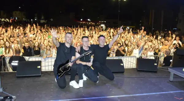 Trzech muzyków na scenie, z gitarą i mikrofonem, pozuje przed rozentuzjazmowanym tłumem. To z pewnością udane imieniny Jana!