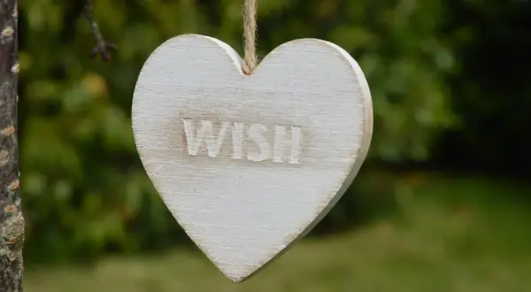 Drewniane serce z napisem "WISH" wisi na sznurku. Idealne na życzenia urodzinowe dla podróżnika, by spełniły się jego marzenia o dalekich wyprawach.