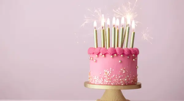 Różowy tort z gwiazdkami i złotymi świeczkami, ozdobiony różową posypką, z iskrami fajerwerków. Idealny na piękne życzenia urodzinowe.