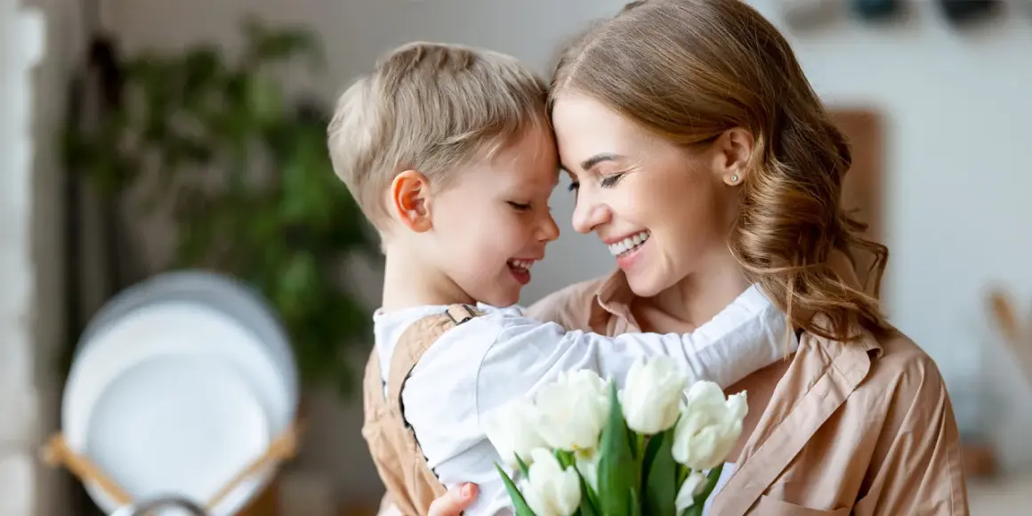 Uśmiechnięta mama i synek przytulają się, trzymając bukiet białych tulipanów. Idealny prezent na 26 maja, Dzień Matki.