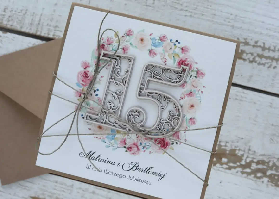 Elegancka kartka z napisem "15 rocznica ślubu" dla Malwiny i Bartłomieja, ozdobiona kwiatowym wianuszkiem i przewiązana sznurkiem.