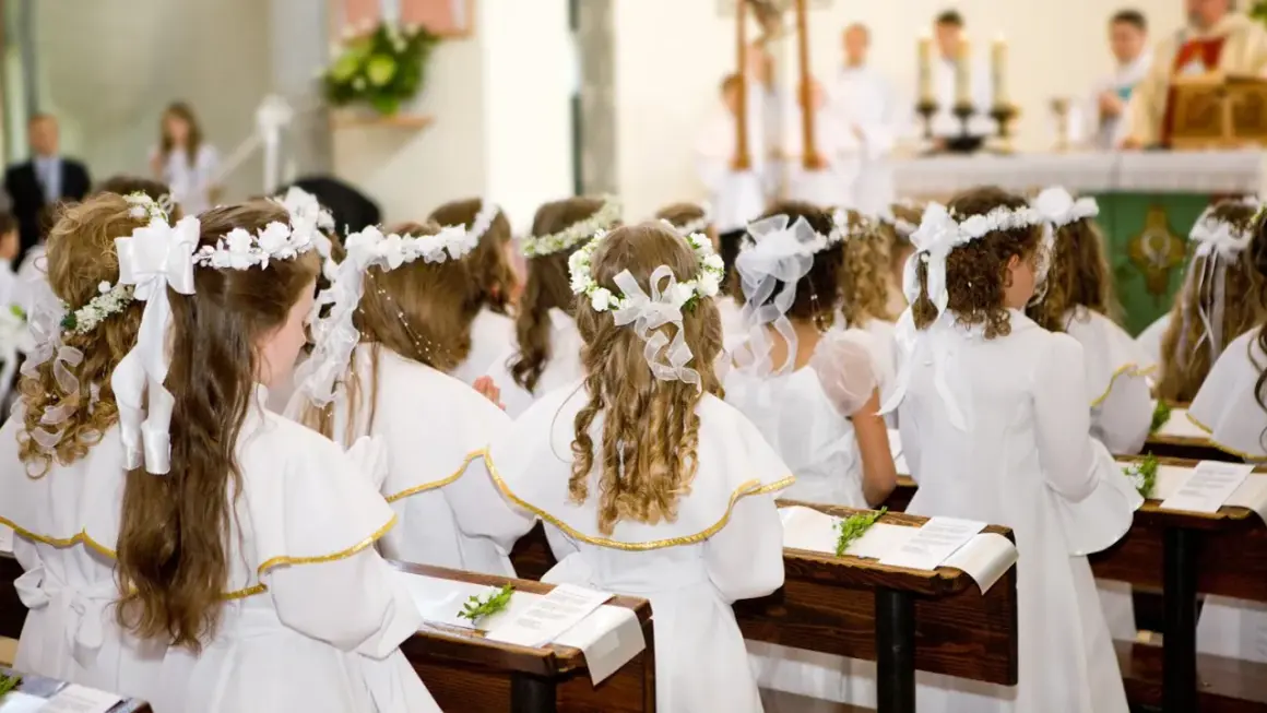Dziewczynki w bieli, z wiankami na głowach, czekają na uroczystość. Krótkie życzenia na komunię dla nich.