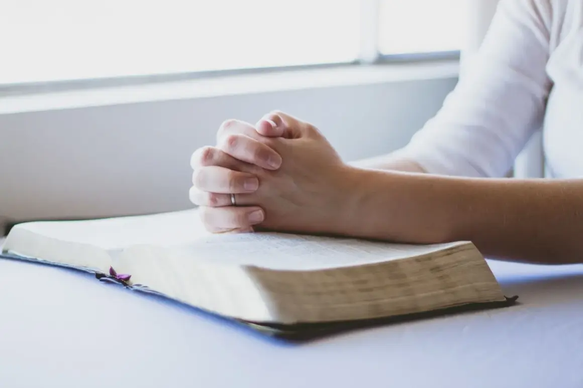Dłonie złożone w modlitwie nad otwartą Biblią. To chwila głębokiej wiary i modlitwa o zdrowie dziecka.