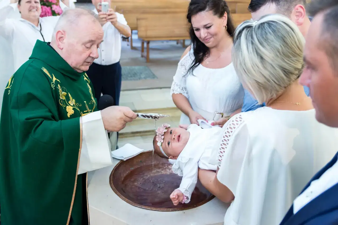 Uroczysty chrzest dziecka w kościele. Kapłan polewa główkę niemowlęcia wodą święconą.